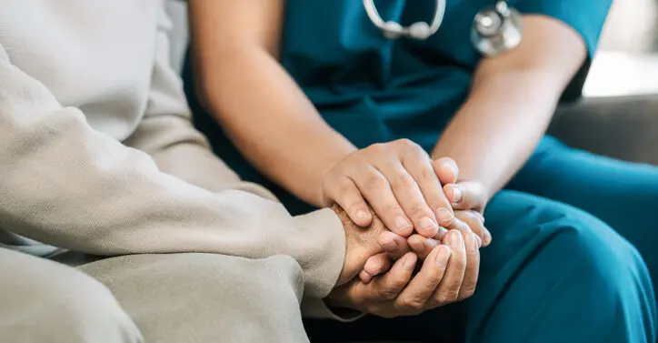 Heimpflege - eine Pflegerin hält einer älteren Dame die Hand