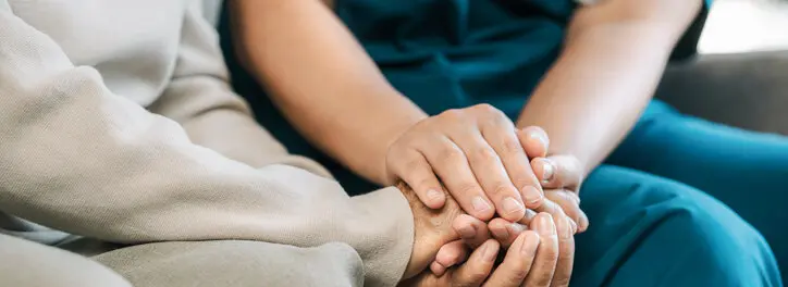 Heimpflege - eine Pflegerin hält einer älteren Dame die Hand